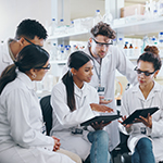 Group of diverse scientists in lab coats reviewing data on digital tablets in a laboratory surrounded by glassware and a microscope.