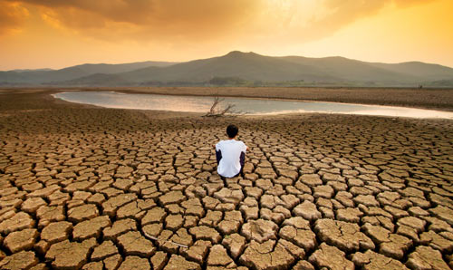 A man sat looking at a small amount of water in an almost dry reservoir